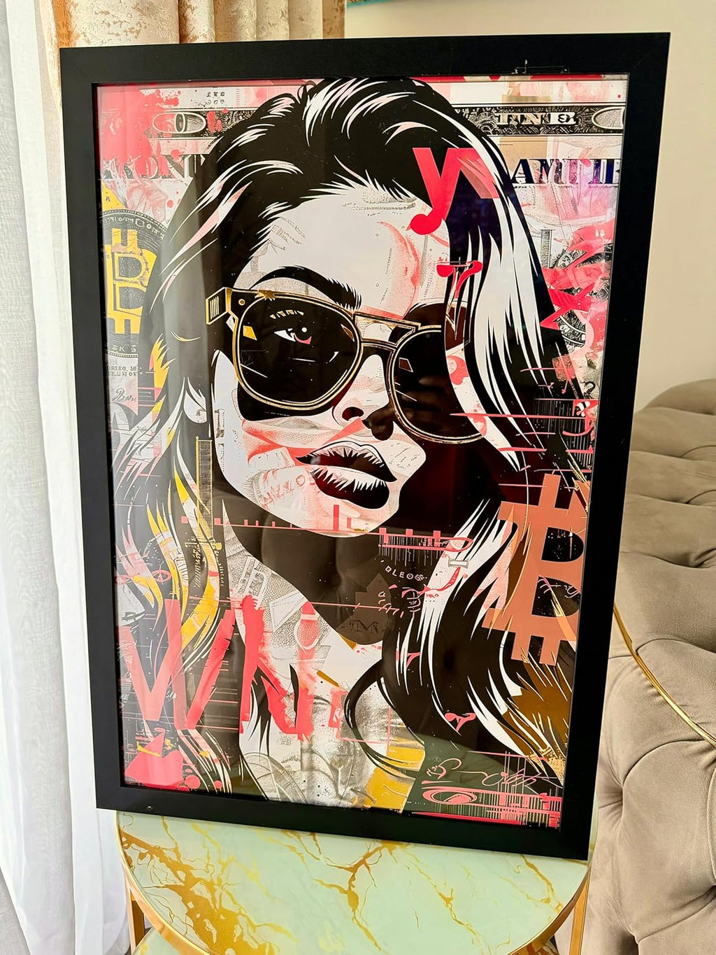Tableau Crypto Couture pose sur une table en marbre avec un canape beige en arriere-plan : portrait pop art de femme en lunettes de soleil, couleurs vives et cadres noir, style street art